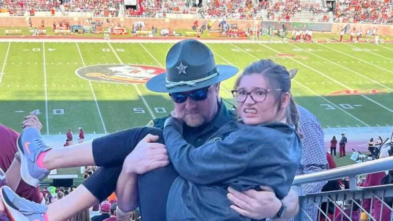 Image of Florida deputy carrying girl struggling to walk up stadium stairs at football game goes viral